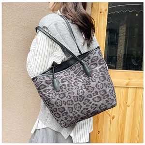Detail view of large leopard print tote bag with black straps on a woman's shoulder