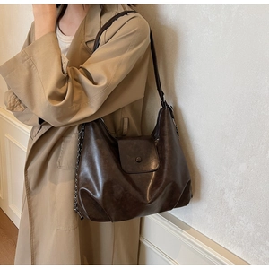 Detail of dark brown leather tote bag with silver chain and metal button on trench coat