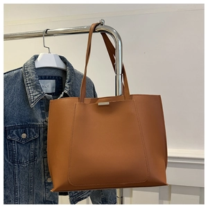 Detail of a brown leather tote bag showing a front pocket and minimalist metal buckle