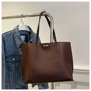 Detail of dark brown tote bag with silver buckle and straps against denim jacket
