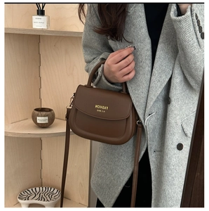 Brown vintage saddle bag with embossed letters and strap shown on a gray wool coat