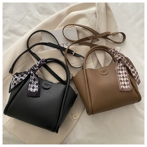Detail view of black and tan bucket bags with litchi grain texture and scarf handles
