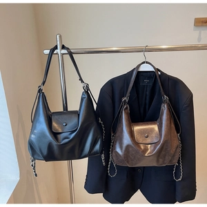 Close-up of minimalist black and dark brown leather tote bags with metal chain details