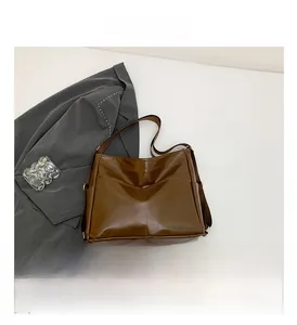 Detailed view of dark brown glossy tote bag with symmetrical stitching and wide shoulder strap