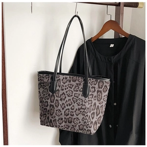 Detail view of large leopard print tote bag with black leather straps hanging on a rack