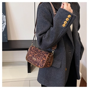 Detail of leopard print cylindrical crossbody bag with brown leather trim and metal label