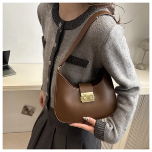 Detail of vintage brown leather underarm bag with gold metal buckle on grey outfit