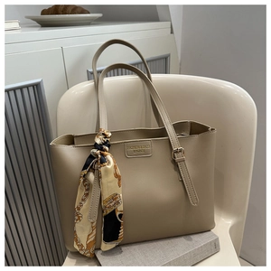 Détail du sac cabas en cuir beige avec foulard décoratif en soie et plaque de logo