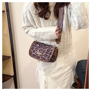 Detail of leopard print cylinder bag with wide woven strap on a white knit sweater