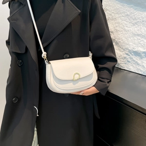Minimalist white faux leather saddle bag with gold metal buckle on a black trench coat