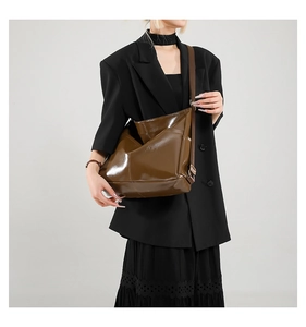 Close-up of brown glossy patent leather hobo bag with adjustable strap on shoulder