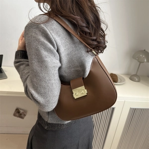 Brown leather half-moon hobo bag with gold metal buckle shown in a lifestyle setting