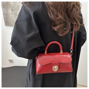 Close-up of red PU leather handbag featuring a gold turn-lock and adjustable shoulder strap