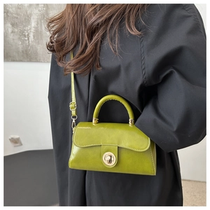 Close-up of avocado green crossbody bag with golden clasp over a black wool coat