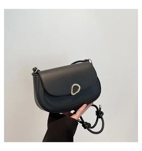 Detail of minimalist black saddle bag with matte leather and a gold irregular metal buckle