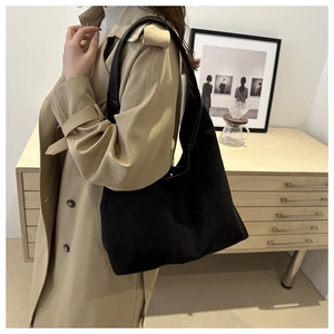 Black suede tote bag with brown straps worn by a model in a beige trench coat