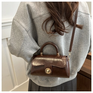 Detail of dark brown retro leather handbag with gold twist lock and crossbody strap