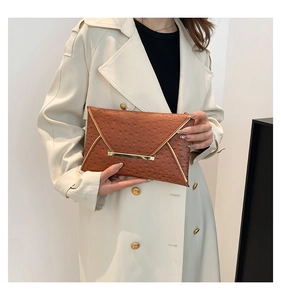 Brown ostrich embossed envelope clutch bag with gold trim held by model in trench coat