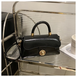 Detail of black glossy handbag with gold metal clasp on a modern metal display stand