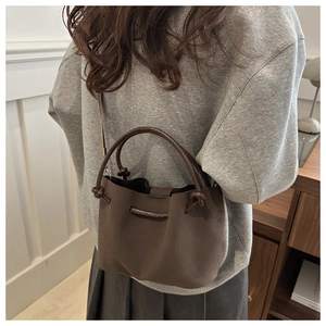 Brown soft leather bucket bag with top handles shown on model in a modern interior