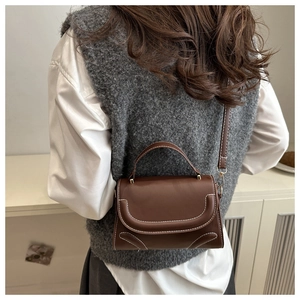 Detail einer braunen Ledertasche mit weißen Kontrastnähten und Tragegriff