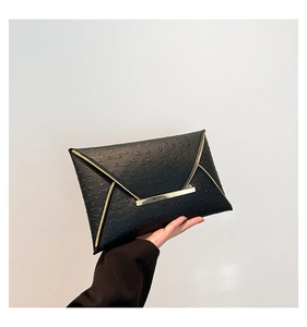 Close-up of black ostrich textured envelope clutch with elegant gold metal trim details