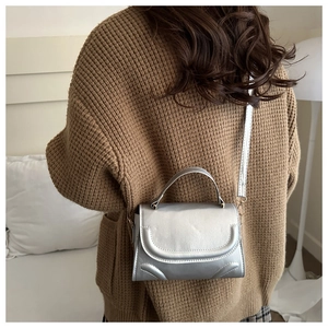 Silberne Metallic-Umhängetasche mit U-Nähten, präsentiert auf einem braunen Pullover
