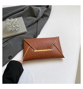 Macro detail of brown ostrich textured envelope clutch with gold metal trim and buckle