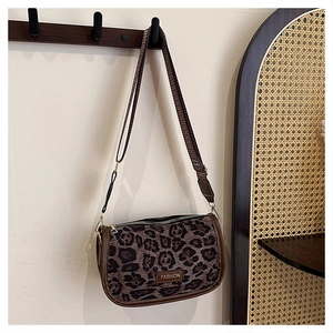 Detail of leopard print crossbody bag with wide strap and fashion logo on beige wall
