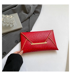Detail of red ostrich embossed leather clutch with gold metal bar on white surface