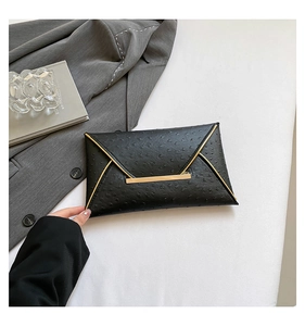 Detail of black ostrich embossed envelope clutch bag with elegant gold metal hardware trim