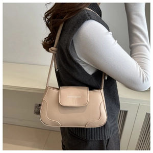 Detail of beige shoulder bag featuring tied strap decoration and embossed fashion text