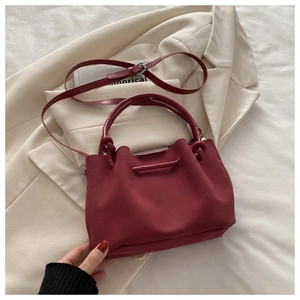 Detail view of a dark red pleated bucket bag placed on a beige blazer with a handle and strap