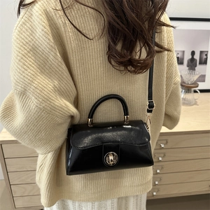 Glossy black square crossbody bag with gold lock for minimalist winter outfits