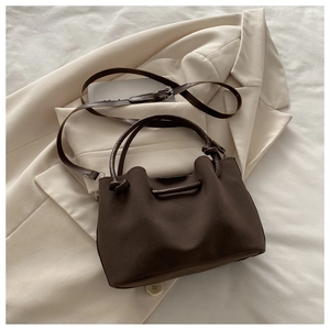 Detail of dark coffee bucket bag with knotted handle on a beige blazer background