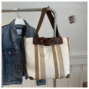 Detail of striped canvas tote bag with brown leather handles and a wide shoulder strap
