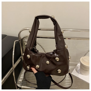 Detail of dark brown glossy patent leather bag featuring silver metal studs and pleats
