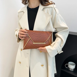 Brown ostrich embossed envelope clutch bag with gold metal trim held by woman in coat