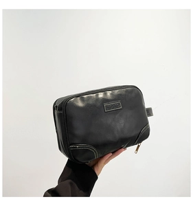Detail of black synthetic leather toiletry bag with white contrast stitching and logo