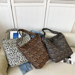 Three leopard print canvas tote bags in white, brown, and grey on a soft sofa