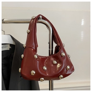 Detail of burgundy patent leather crescent bag with oversized silver studs on handle