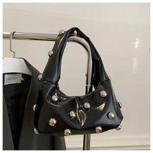 Close-up of black patent leather crescent bag with large silver spherical rivets