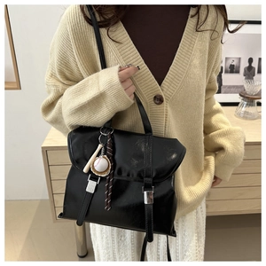 Dettaglio della borsa in ecopelle nera con fibbie decorative e un ciondolo da baseball