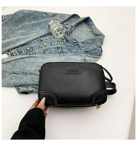 Detail view of black square bag with white contrast stitching and minimalist metal logo