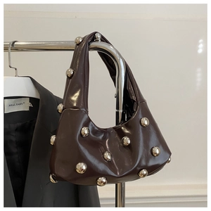 Detail of dark brown patent leather hobo bag with silver rivet studs on a metal hanger