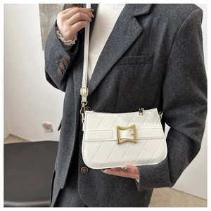 Gros plan d'un sac bandoulière blanc matelassé avec boucle dorée sur un costume gris
