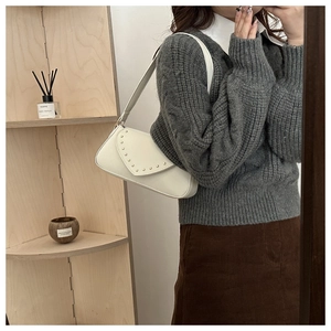 Chic beige leather shoulder bag with decorative rivet edge trim shown in a modern interior