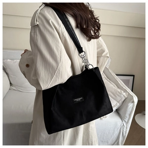 Detail of minimalist black tote bag featuring silver chain strap and leather logo patch
