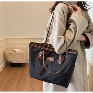 Close-up of black nylon tote bag with brown leather handles and brand logo tag