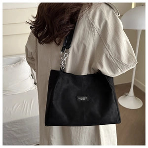 Detail of minimalist black tote bag with silver chain strap and leather patch logo